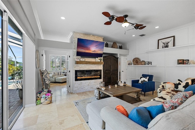 living room with visible vents, a ceiling fan, crown molding, a stone fireplace, and a decorative wall