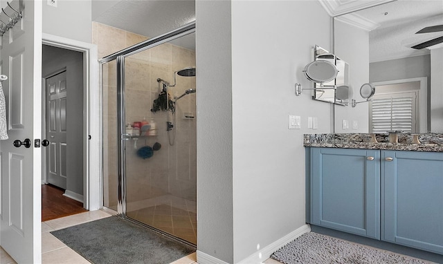 full bathroom with a stall shower, tile patterned flooring, baseboards, and vanity