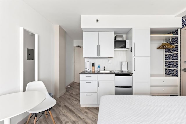 kitchen featuring light hardwood / wood-style flooring, electric panel, stainless steel refrigerator, sink, and white cabinetry