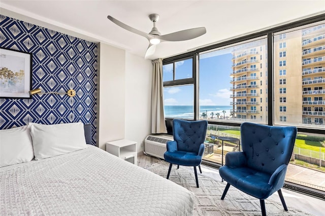 bedroom featuring wood-type flooring, a water view, a wall unit AC, a wall of windows, and ceiling fan