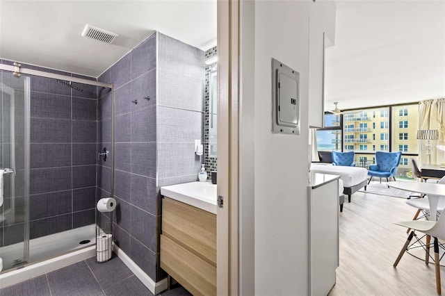 bathroom featuring a shower with door, electric panel, expansive windows, tile walls, and vanity