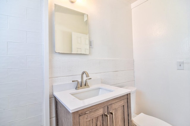 half bathroom featuring toilet, tile walls, and vanity