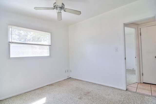 empty room with a ceiling fan, baseboards, and speckled floor