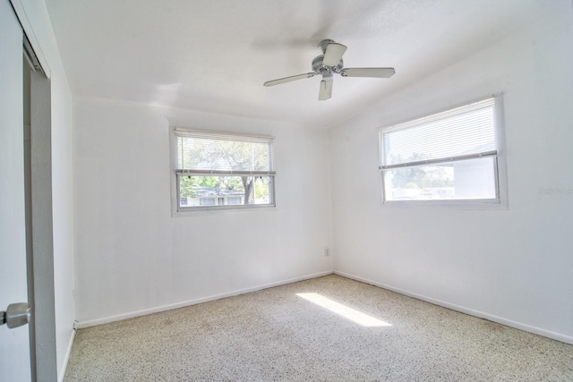 empty room with ceiling fan, baseboards, and speckled floor