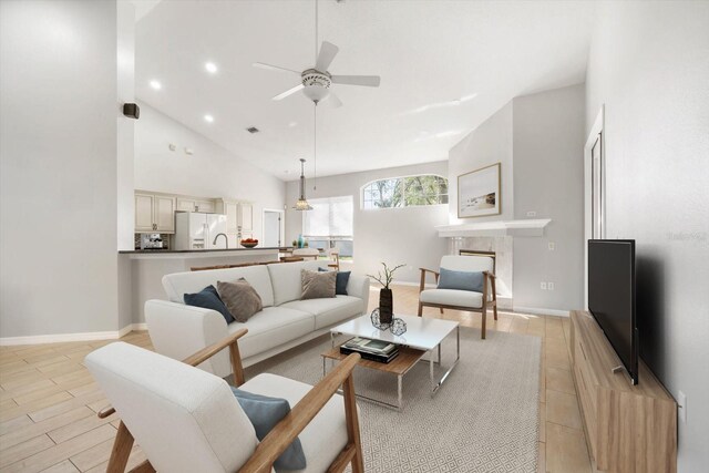 living room featuring high vaulted ceiling, baseboards, a fireplace, and light wood finished floors