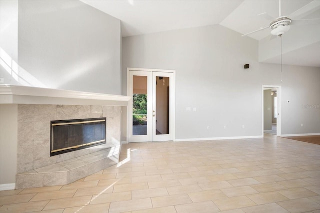 unfurnished living room featuring french doors, ceiling fan, high vaulted ceiling, a tile fireplace, and baseboards