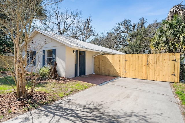 view of side of property featuring metal roof, fence, a gate, and stucco siding