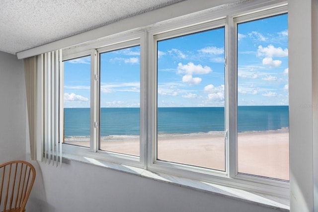 interior space featuring a water view, a beach view, and a textured ceiling