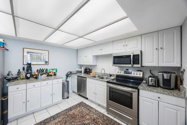 kitchen with decorative backsplash, appliances with stainless steel finishes, white cabinetry, a sink, and light tile patterned flooring