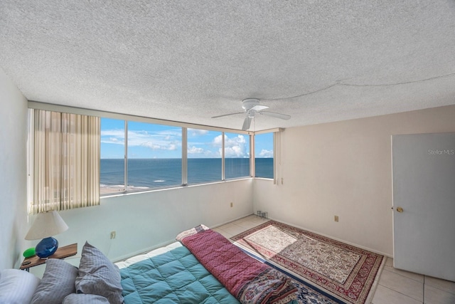 bedroom with a ceiling fan, light tile patterned flooring, a water view, and a textured ceiling