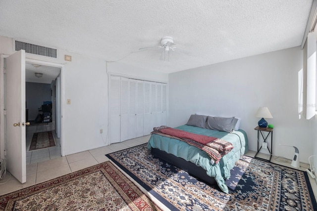 bedroom with light tile patterned floors, a closet, visible vents, a ceiling fan, and a textured ceiling