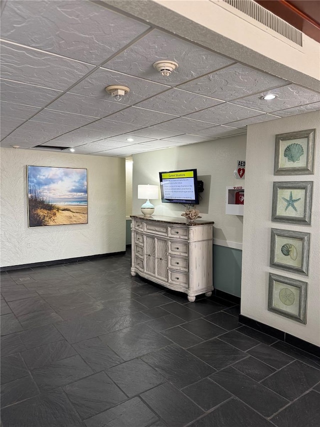 bar with visible vents, a drop ceiling, and baseboards