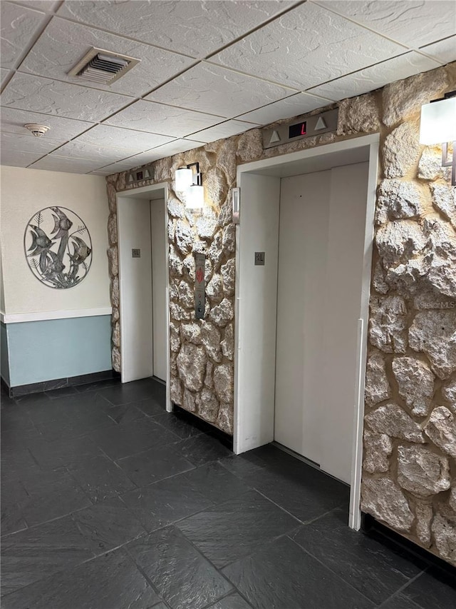 spare room featuring a paneled ceiling, elevator, and visible vents