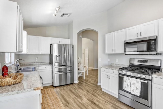 kitchen with sink, stainless steel appliances, vaulted ceiling, and white cabinets