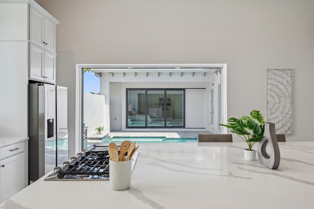 interior space with white cabinets, stainless steel fridge, and light stone counters