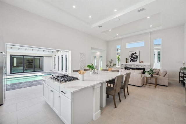 kitchen featuring a center island, light stone countertops, white cabinets, a tiled fireplace, and a raised ceiling