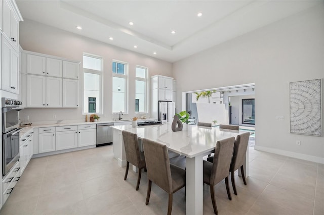 dining space with light tile patterned flooring, a towering ceiling, a tray ceiling, and sink