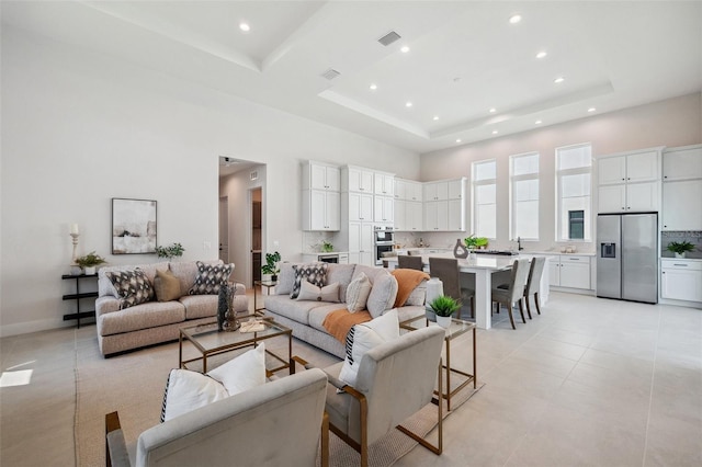 living room with a towering ceiling, a tray ceiling, and light tile patterned floors