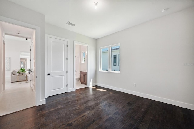 unfurnished bedroom featuring multiple windows, ensuite bathroom, and dark wood-type flooring