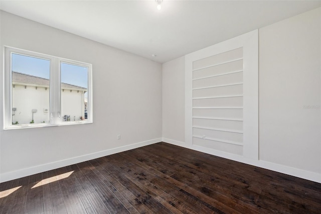 spare room with built in shelves and dark hardwood / wood-style floors