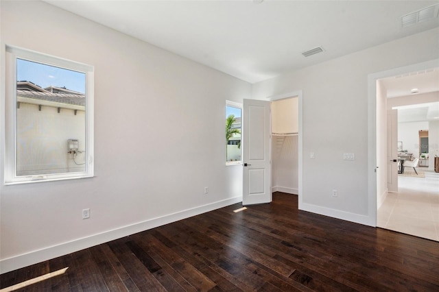 unfurnished bedroom featuring multiple windows, a closet, a spacious closet, and dark hardwood / wood-style floors