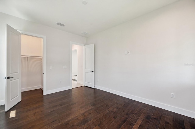 unfurnished bedroom featuring a spacious closet, dark wood-type flooring, and a closet