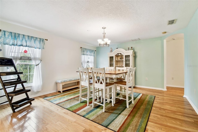 dining area featuring a textured ceiling, plenty of natural light, a notable chandelier, and light hardwood / wood-style floors