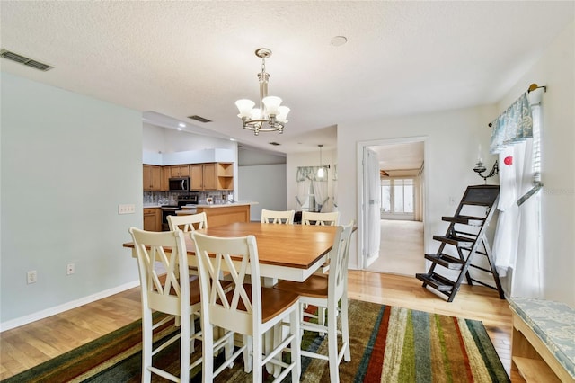 dining area with a textured ceiling, vaulted ceiling, an inviting chandelier, and light hardwood / wood-style floors