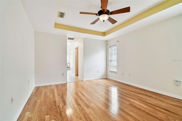 spare room featuring a tray ceiling, ceiling fan, and light hardwood / wood-style floors