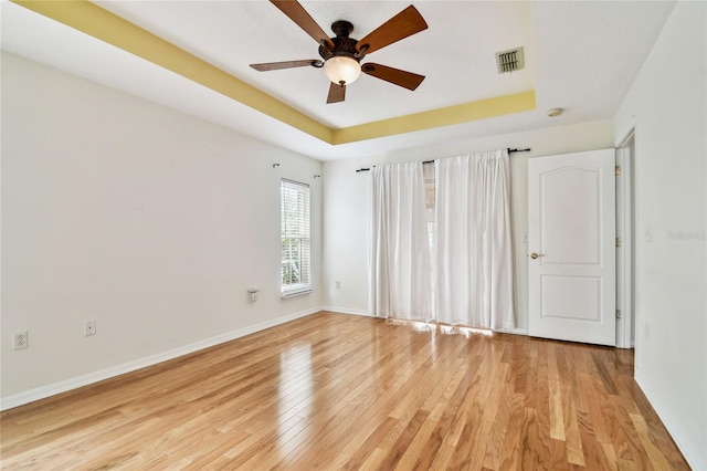 unfurnished room featuring a tray ceiling, ceiling fan, and light hardwood / wood-style floors