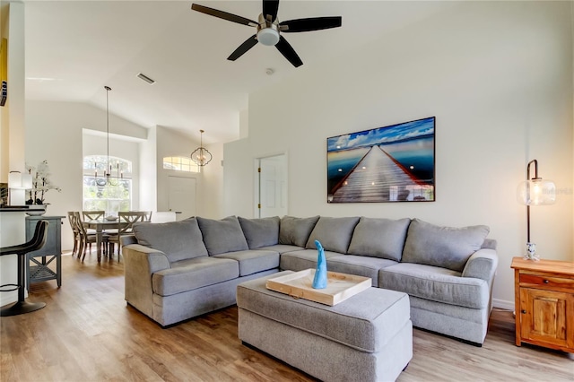 living room featuring ceiling fan with notable chandelier, high vaulted ceiling, and light hardwood / wood-style flooring