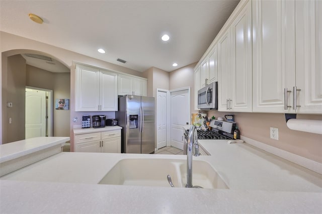 kitchen with arched walkways, light countertops, appliances with stainless steel finishes, and white cabinets