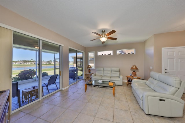 living room with light tile patterned floors, a water view, a ceiling fan, a textured ceiling, and baseboards