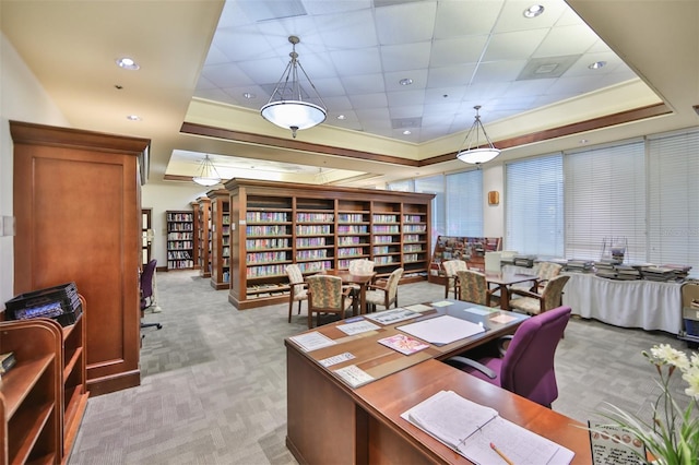 office space with wall of books, a raised ceiling, and light colored carpet