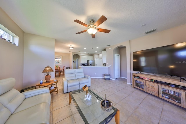 living room featuring arched walkways, light tile patterned floors, visible vents, a textured ceiling, and baseboards