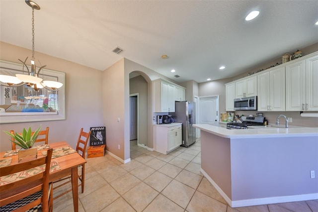 kitchen with decorative light fixtures, a peninsula, stainless steel appliances, light countertops, and white cabinetry