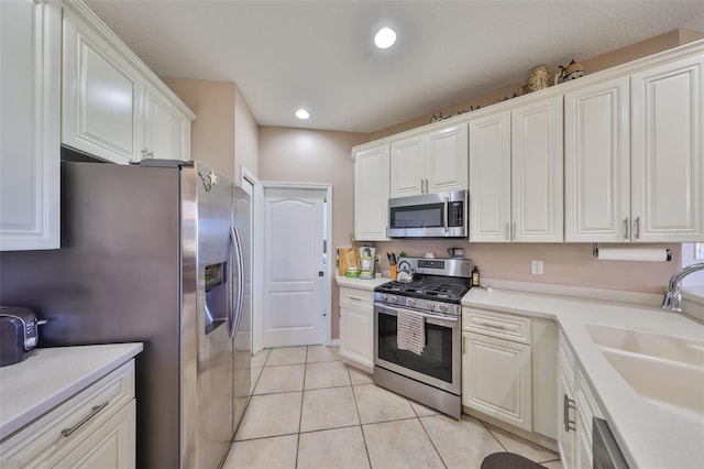 kitchen with light tile patterned flooring, a sink, white cabinetry, light countertops, and appliances with stainless steel finishes