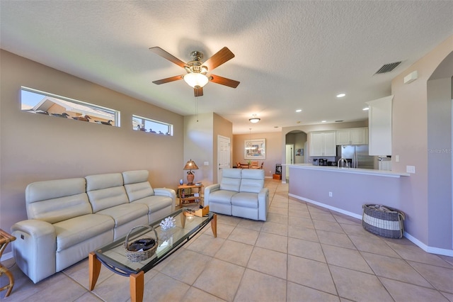 living room with arched walkways, light tile patterned floors, visible vents, a ceiling fan, and baseboards