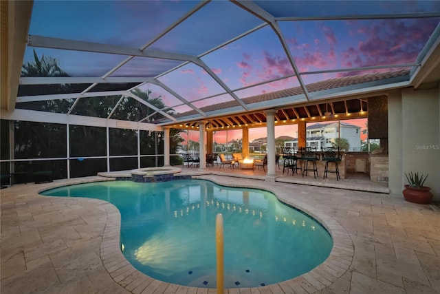 pool at dusk with outdoor dry bar, a patio, glass enclosure, and a pool with connected hot tub