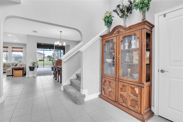 stairway featuring a chandelier, baseboards, arched walkways, and tile patterned floors