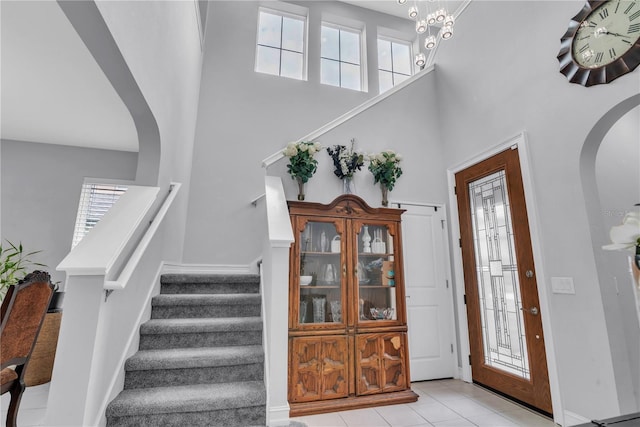 foyer featuring arched walkways, light tile patterned floors, a towering ceiling, and stairs