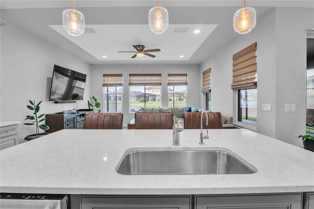 kitchen with gray cabinetry, a sink, open floor plan, hanging light fixtures, and a center island with sink