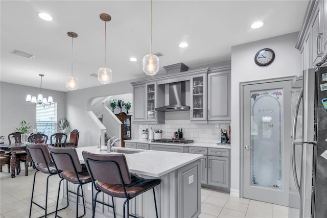 kitchen featuring glass insert cabinets, decorative light fixtures, wall chimney range hood, and gray cabinetry