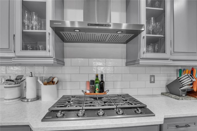 kitchen with range hood, stainless steel gas cooktop, gray cabinets, light countertops, and glass insert cabinets