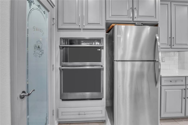 kitchen featuring stainless steel appliances, gray cabinets, light countertops, and decorative backsplash