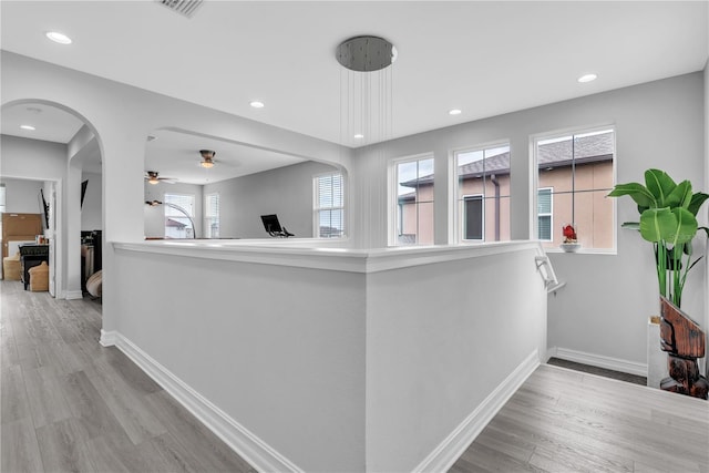 hallway featuring arched walkways, light wood finished floors, recessed lighting, and baseboards