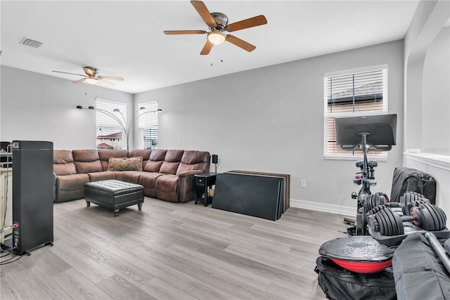 living room featuring light wood-style flooring, a ceiling fan, visible vents, and baseboards