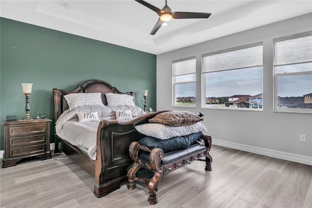 bedroom featuring light wood-style floors, a tray ceiling, baseboards, and a ceiling fan