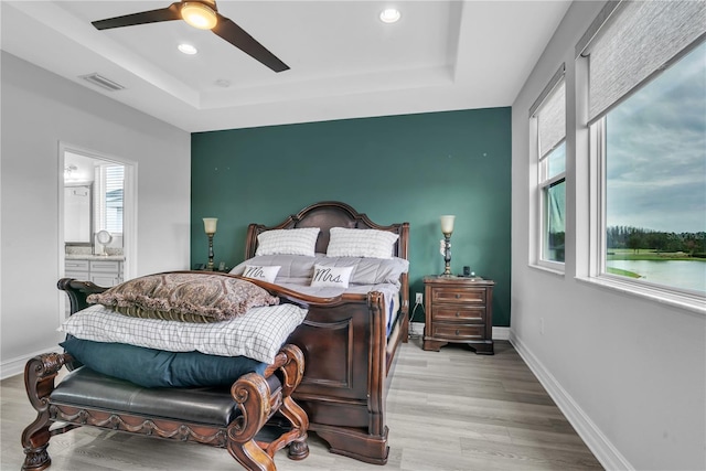 bedroom featuring a tray ceiling, light wood-type flooring, visible vents, and baseboards