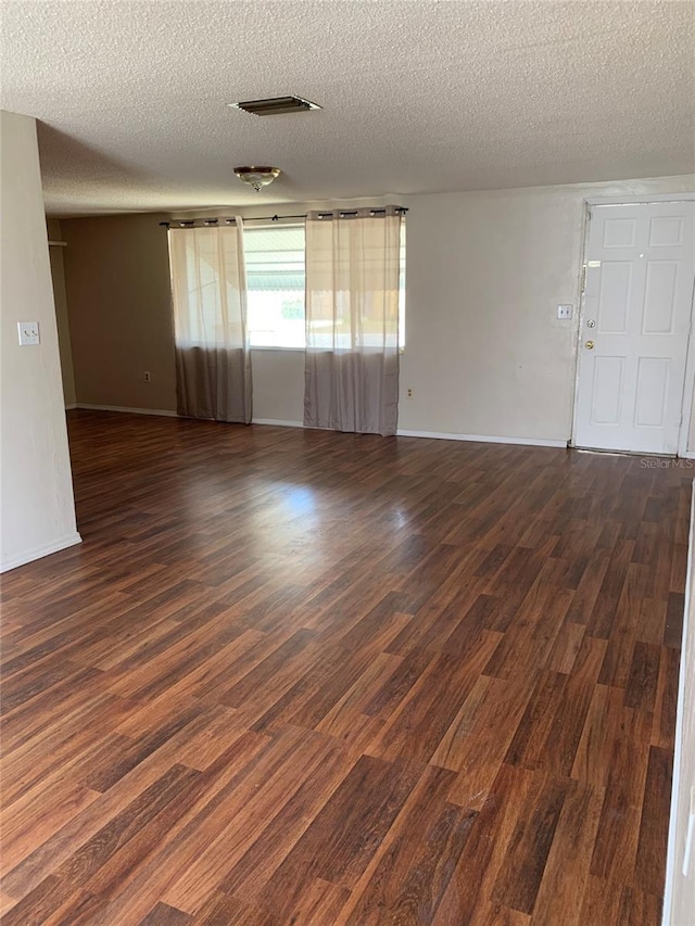 empty room with a textured ceiling, baseboards, and dark wood-style flooring